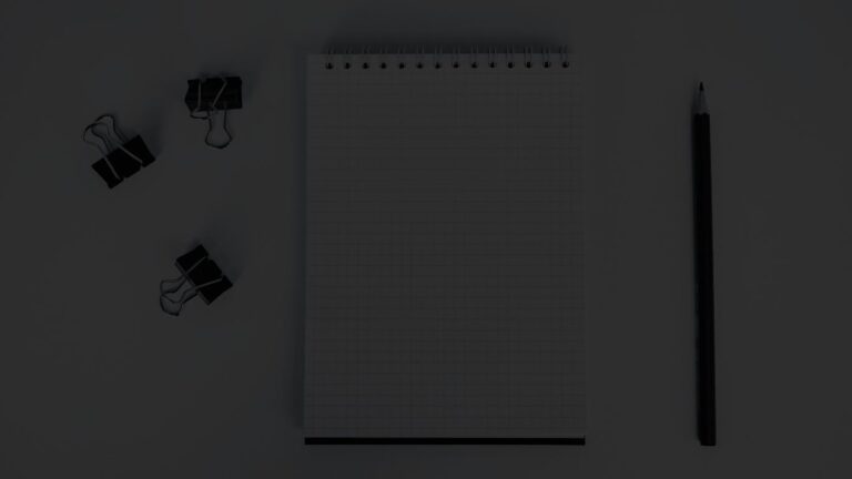 Overhead view of a graph notebook, binder clips, and a pencil