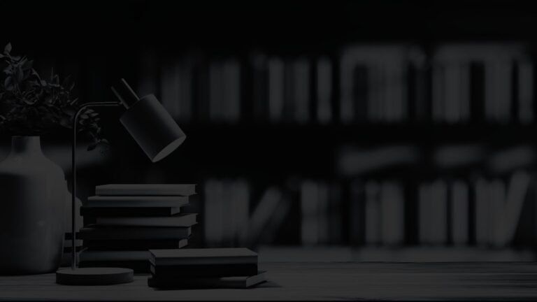 Desk lamp and stacked books in focus against a softly blurred bookshelf