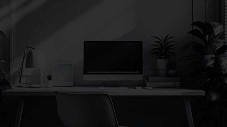 Large desktop computer, table lamp, and small house plant on simple wooden desk