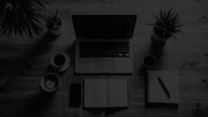 Top-down view of a MacBook, coffee cups, notepad, and smartphone on a simple wooden surface