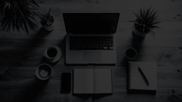 Top-down view of a MacBook, coffee cups, notepad, and smartphone on a simple wooden surface