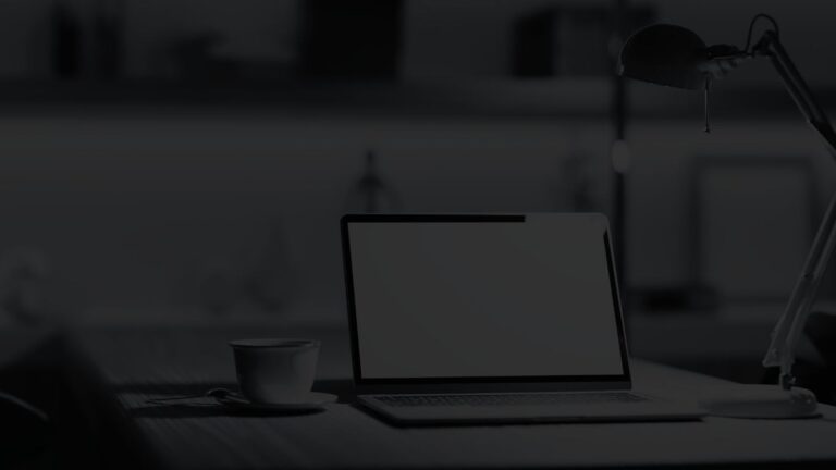 Open laptop between a modern desk lamp and a cup of coffee