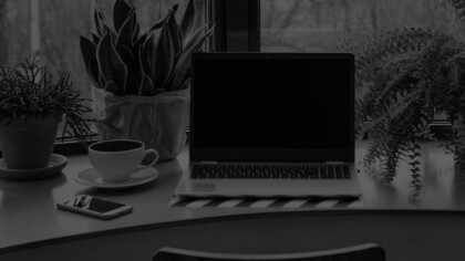 a laptop, plant, phone and cup of coffee sitting on a disk