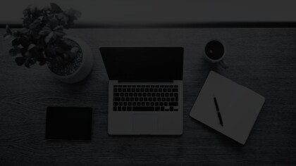 Top down view of an open laptop, notebook, cup of coffee, tablet, and house plant