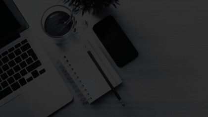 Angled overhead view of a workspace with a laptop, notebook, pen, smartphone, coffee, and plant