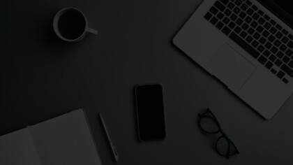 Top view of a laptop, reading glasses, smartphone, and coffee mug