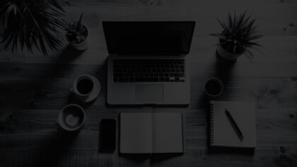 Top-down view of a MacBook, coffee cups, notepad, and smartphone on a simple wooden surface