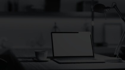 Open laptop between a modern desk lamp and a cup of coffee